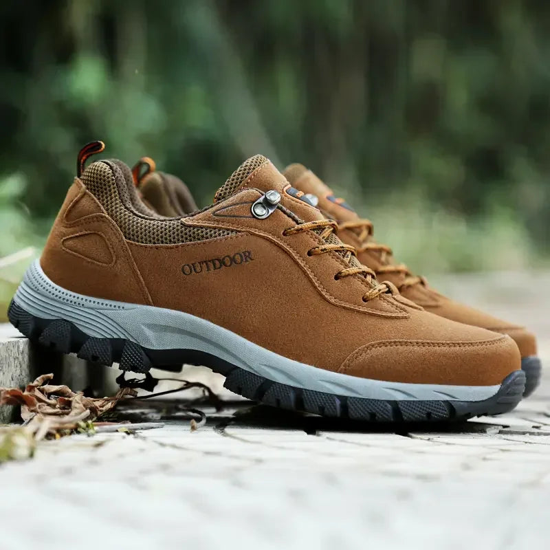 Pair of brown men's hiking shoes displayed outdoors showing rugged tread and durable construction